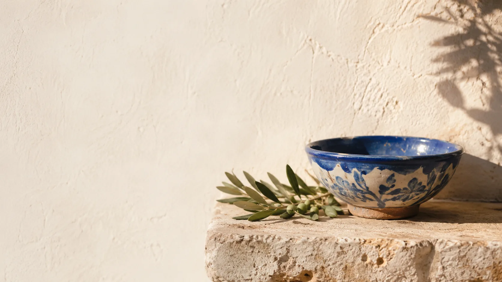 A single cobalt-glazed ceramic bowl on a sunlit limestone ledge.